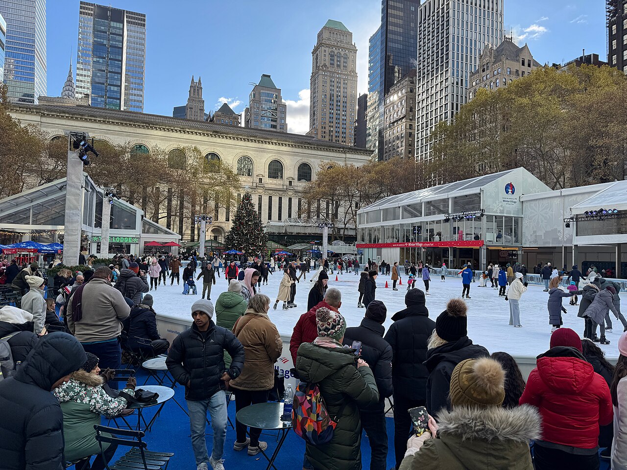 Skaters on the rink at Bryant Park's Winter Village with the New York Public Library and Midtown towers behind