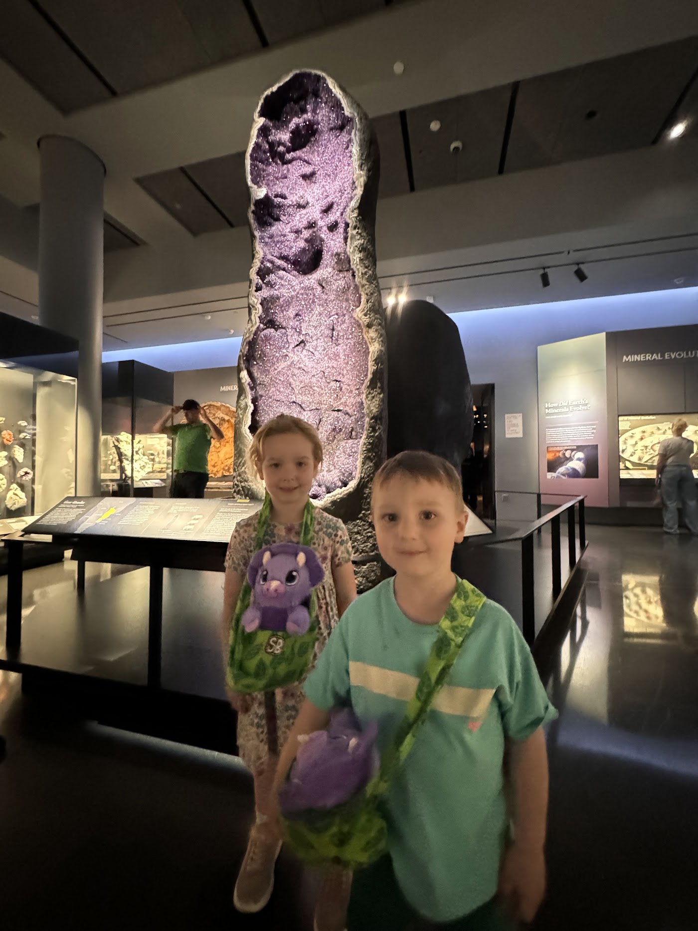 Two children beside a purple amethyst geode taller than they are.
