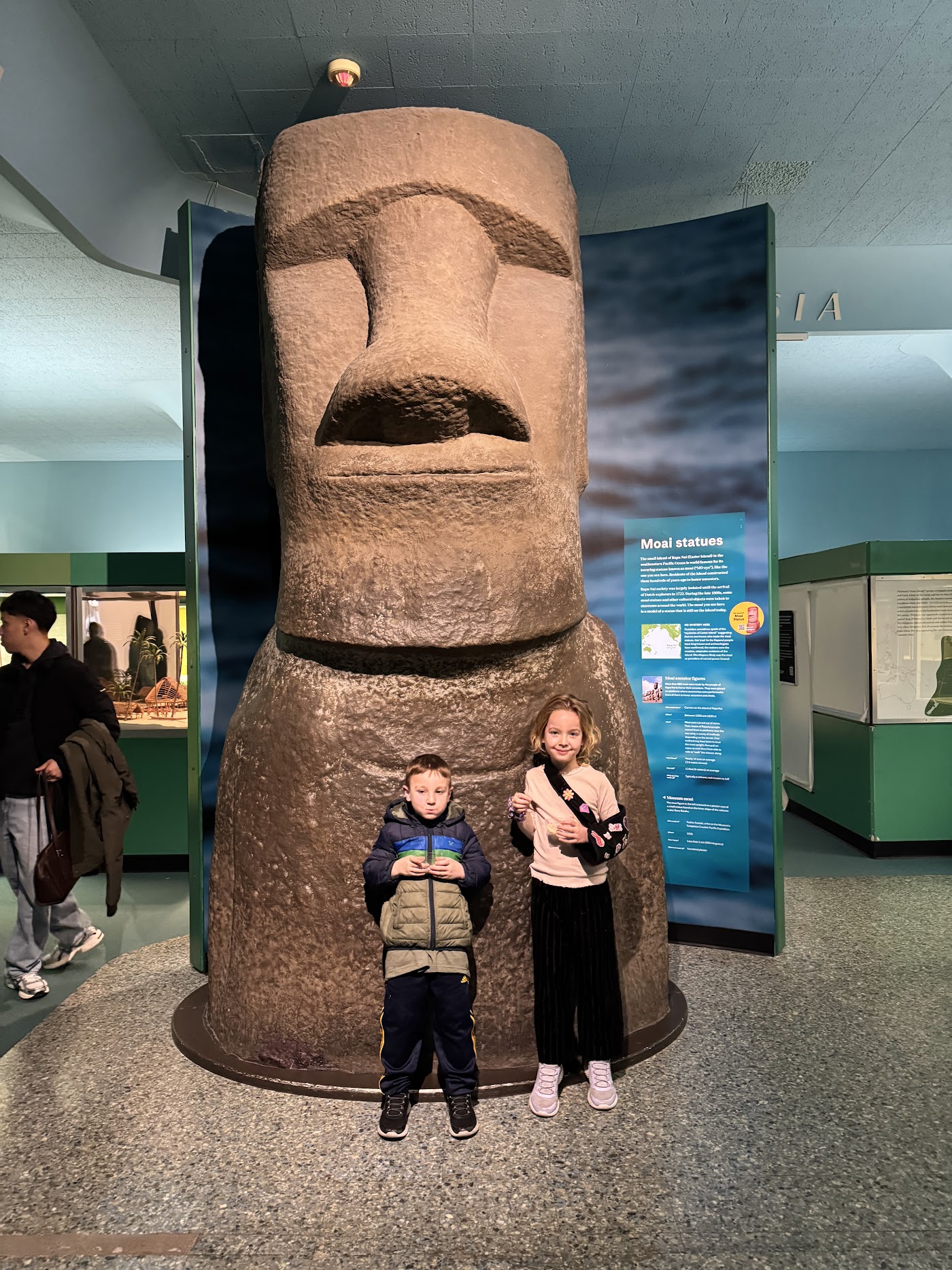 Two children beside a tall stone head, a cast of an Easter Island moai.