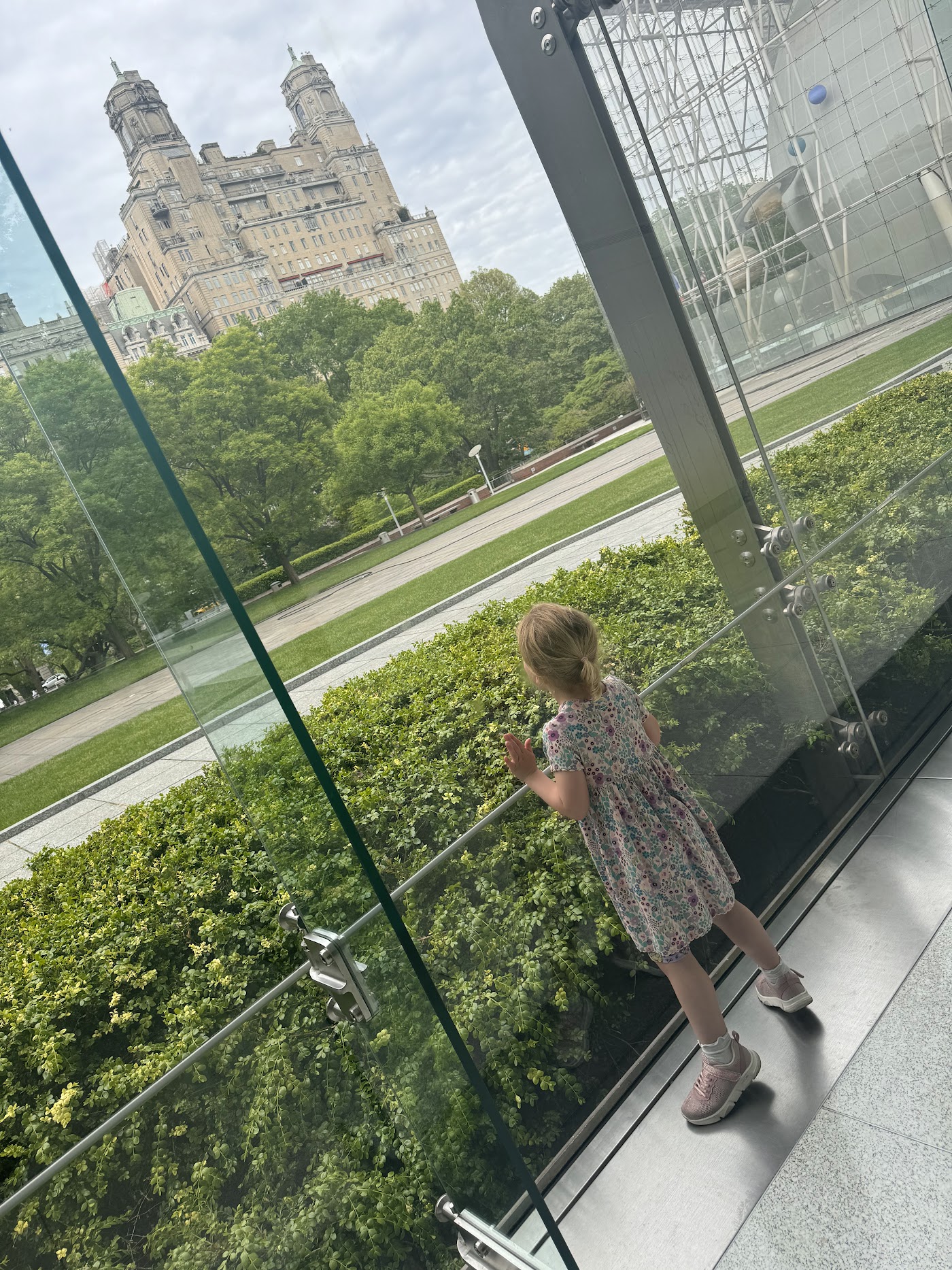 A child at a floor-to-ceiling window with the trees of Central Park below.