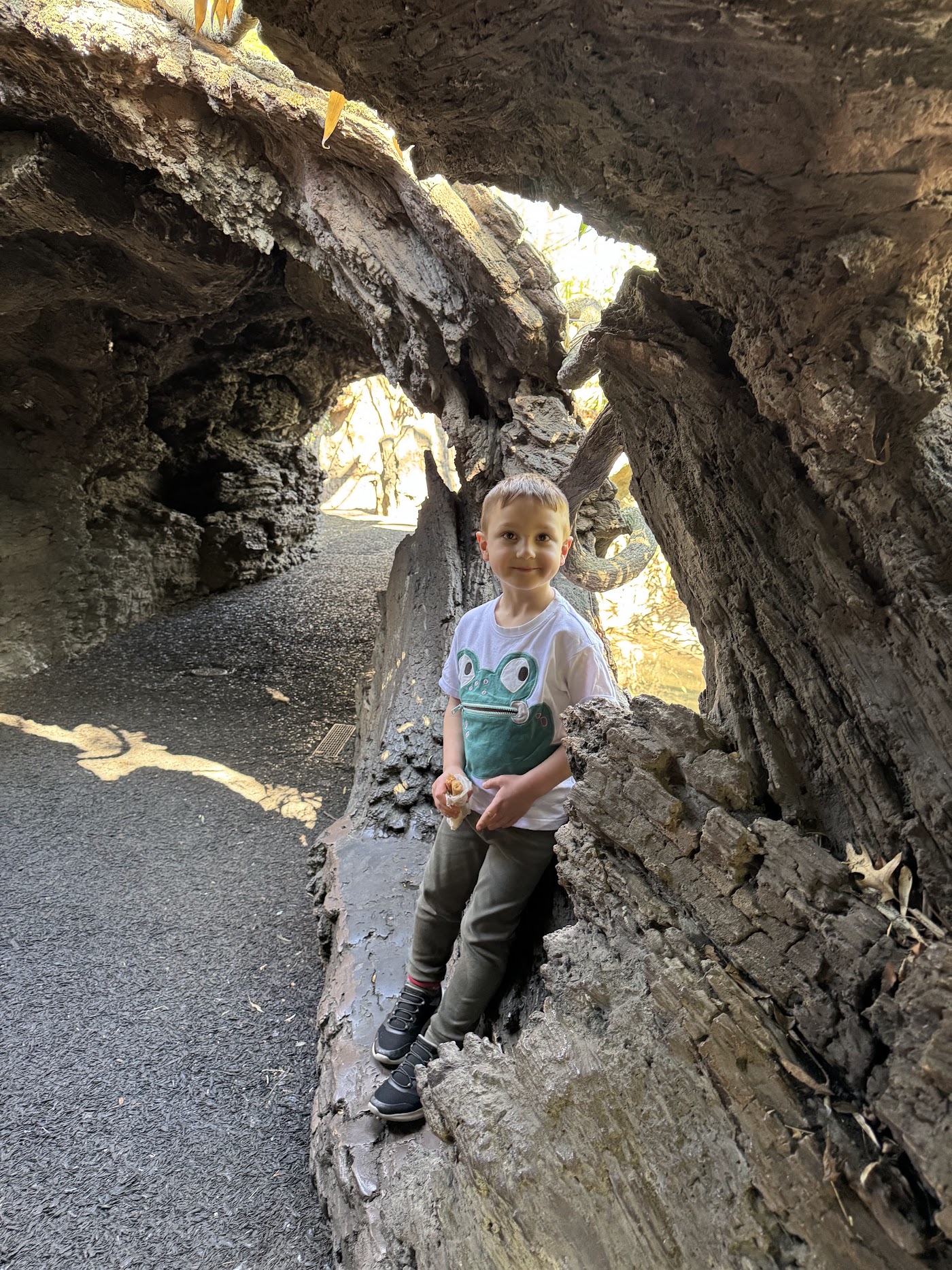 A girl in a pink jacket inside a hollow fake tree trunk.