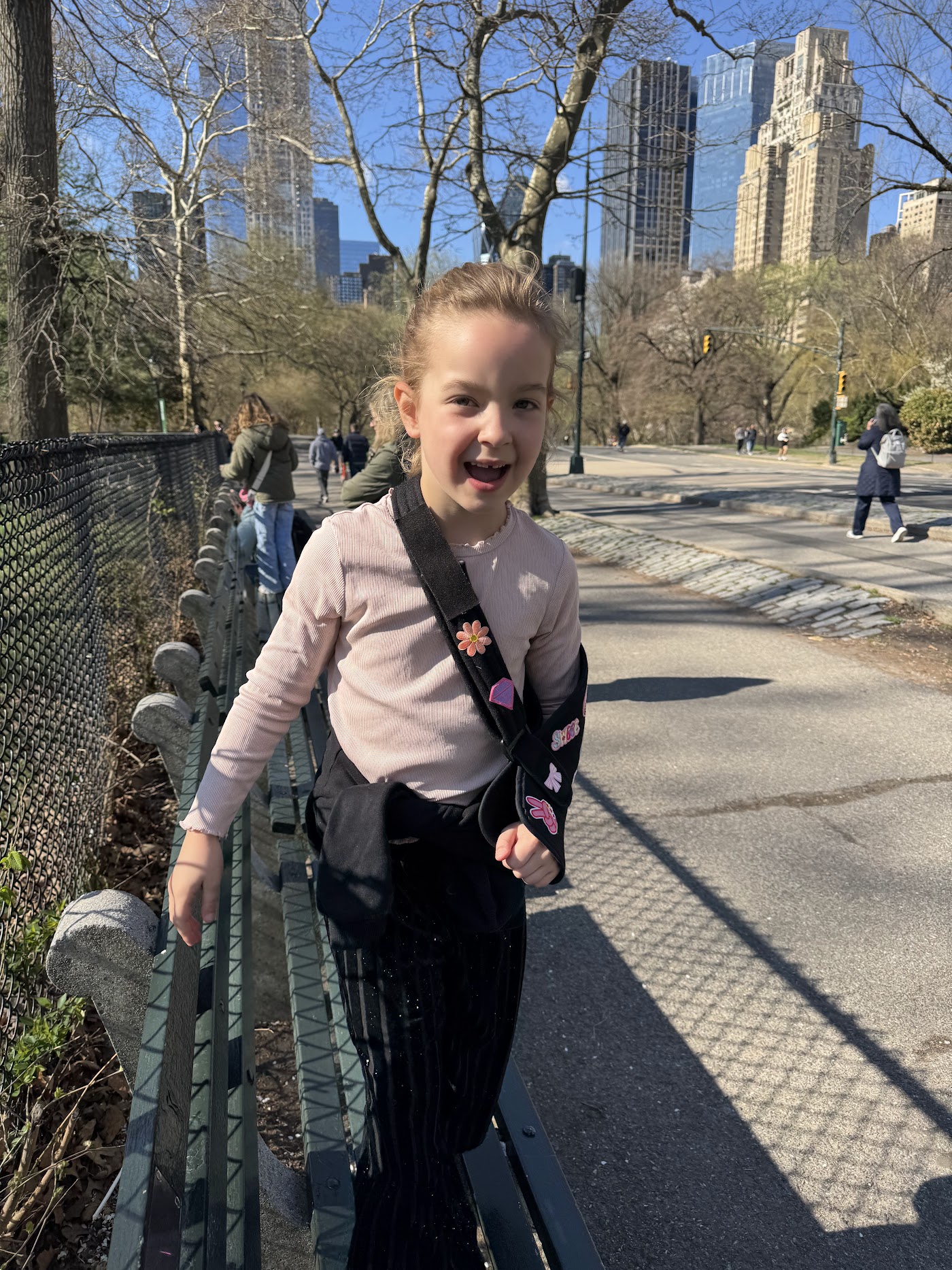 A girl on a park path with bare trees and skyscrapers behind.