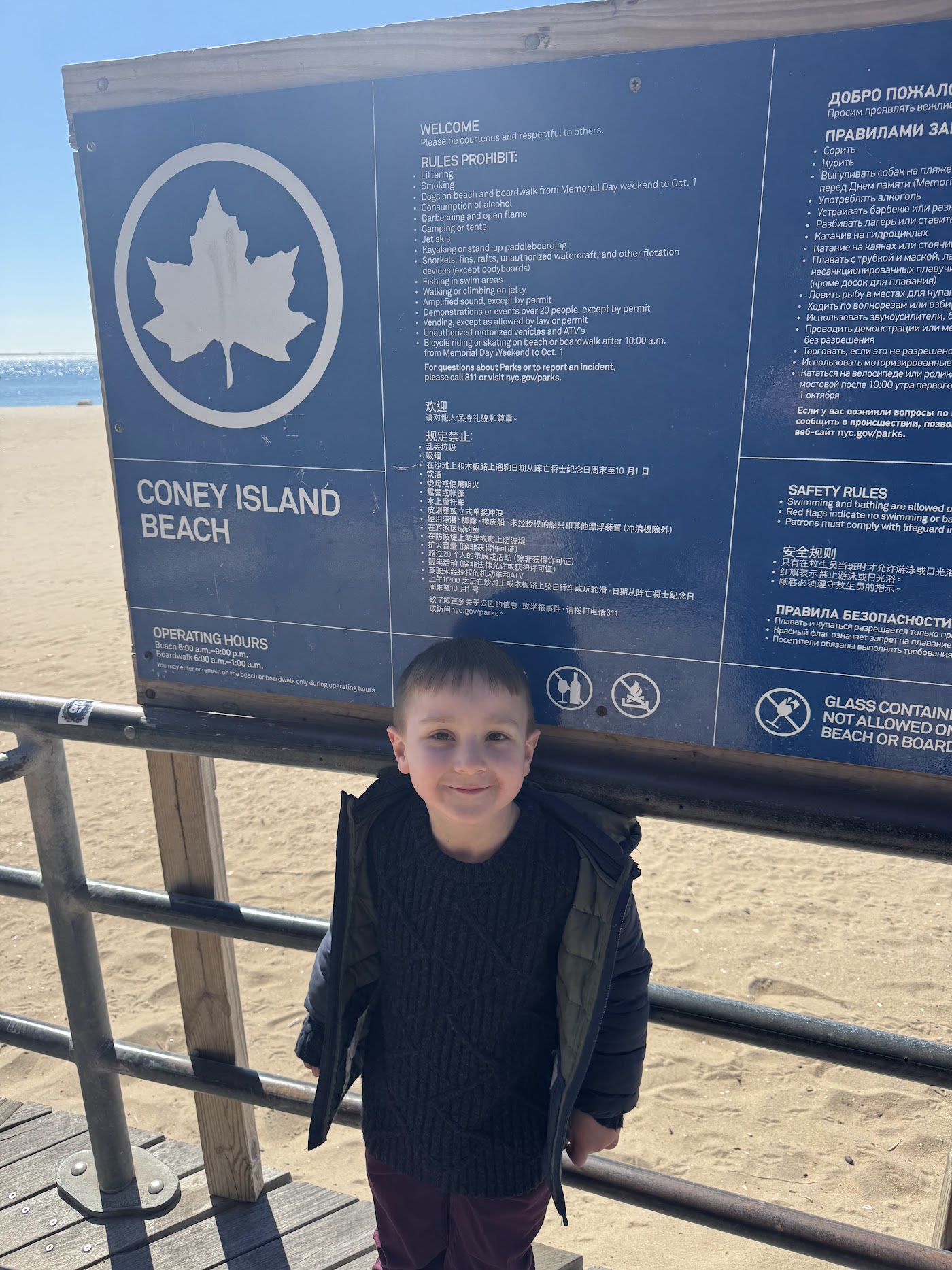 A child in front of a blue NYC Parks sign for Coney Island Beach.