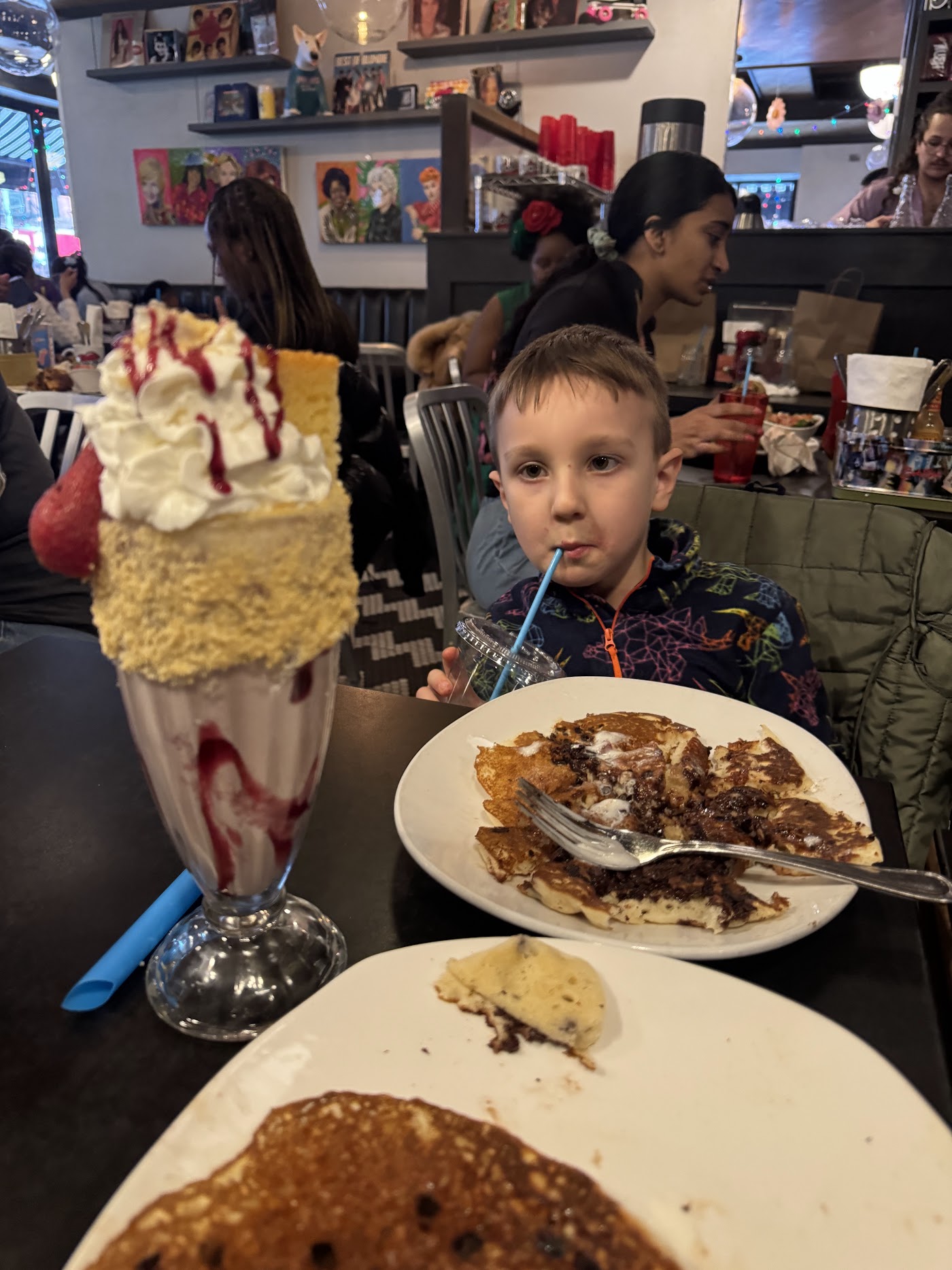 A boy at a diner table with a stack of pancakes and a tall milkshake.
