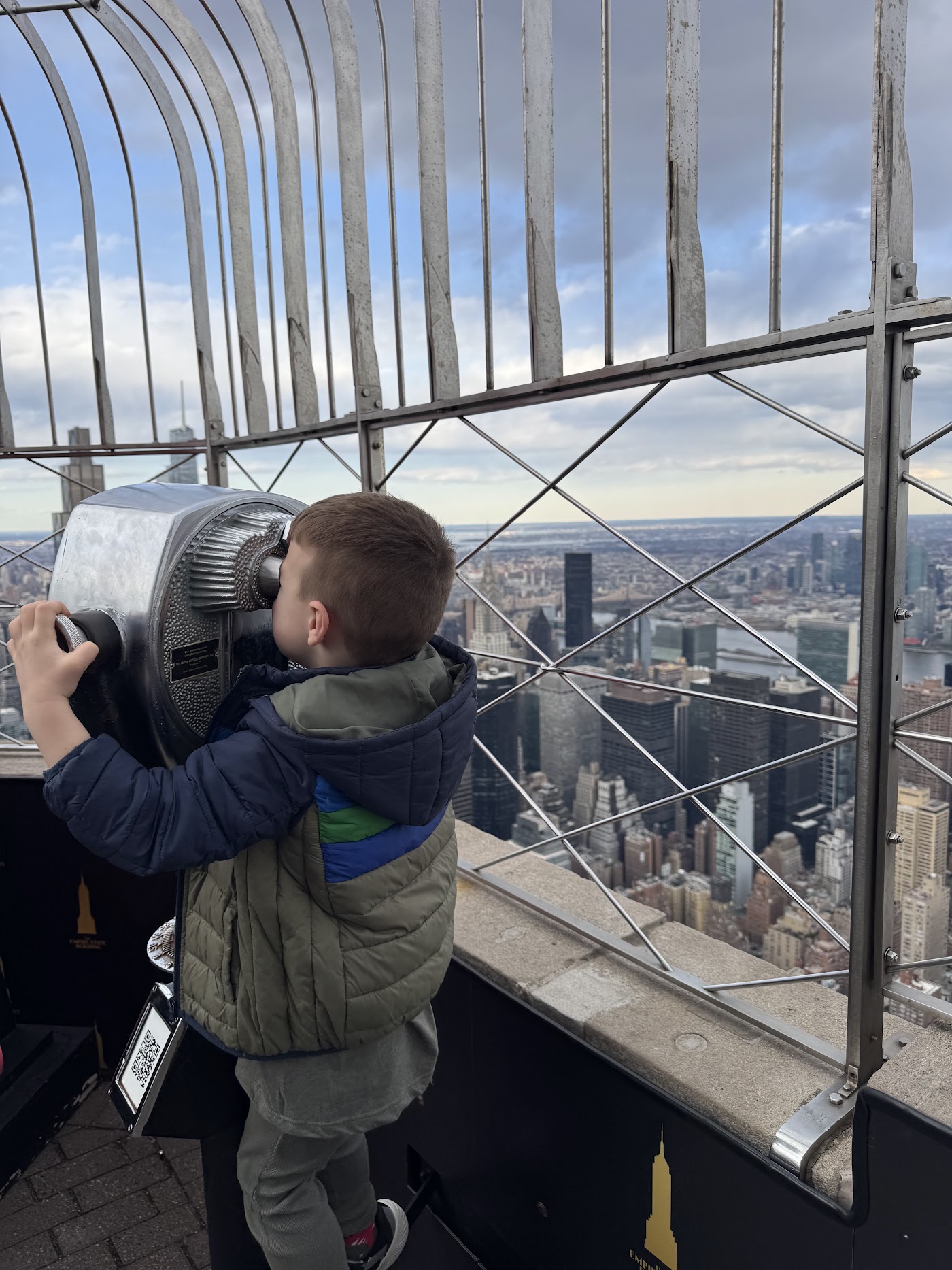 A child looking through a silver coin-operated viewer with the city below.