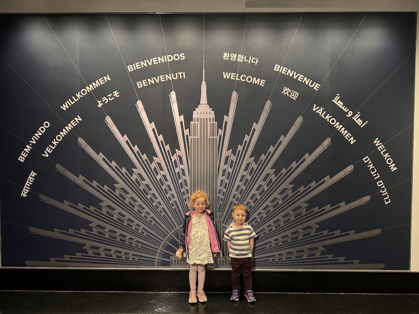 Two children in front of a dark wall with the building's outline and welcome messages.