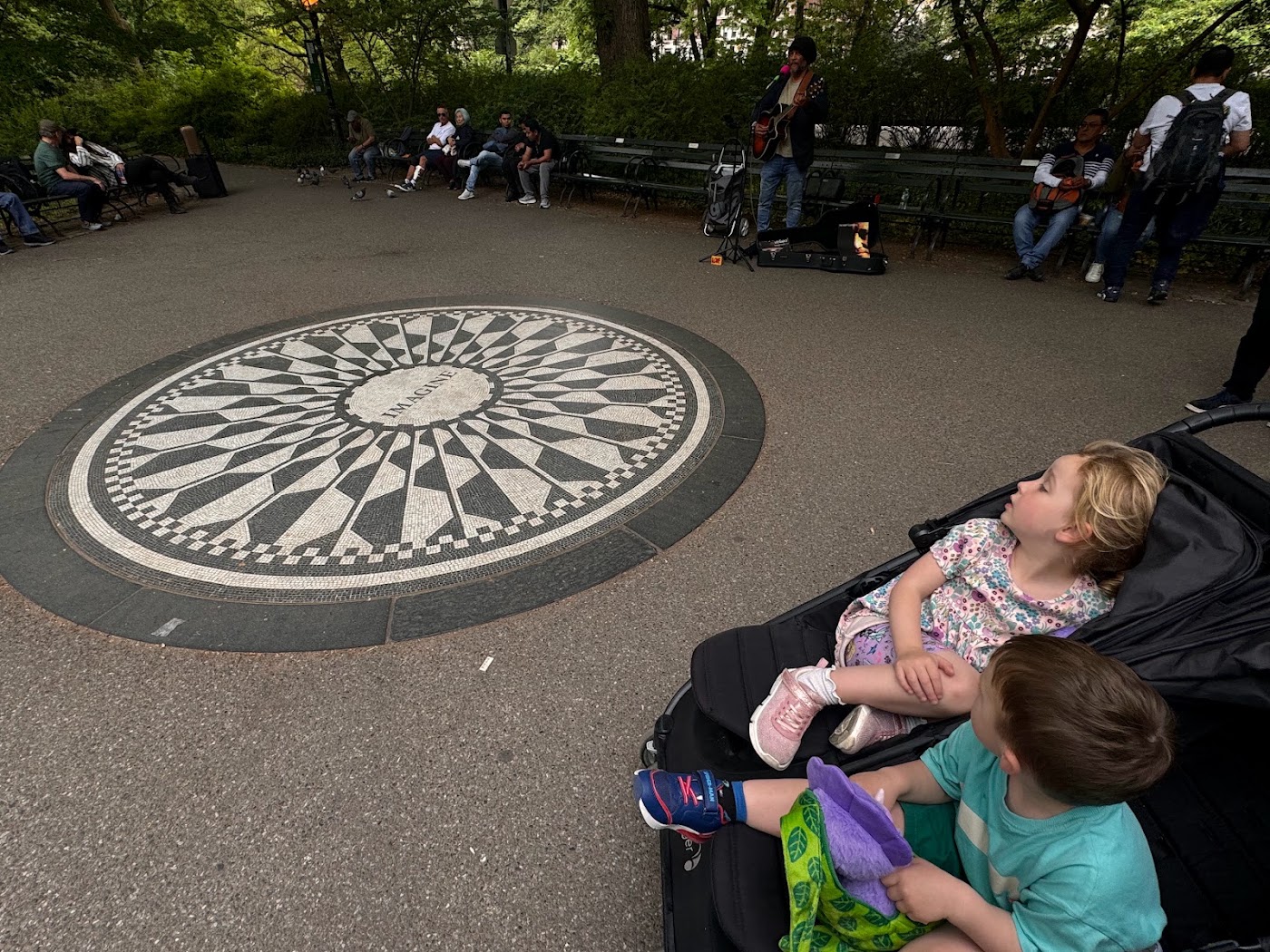 A toddler in a stroller beside the black and white Imagine mosaic.