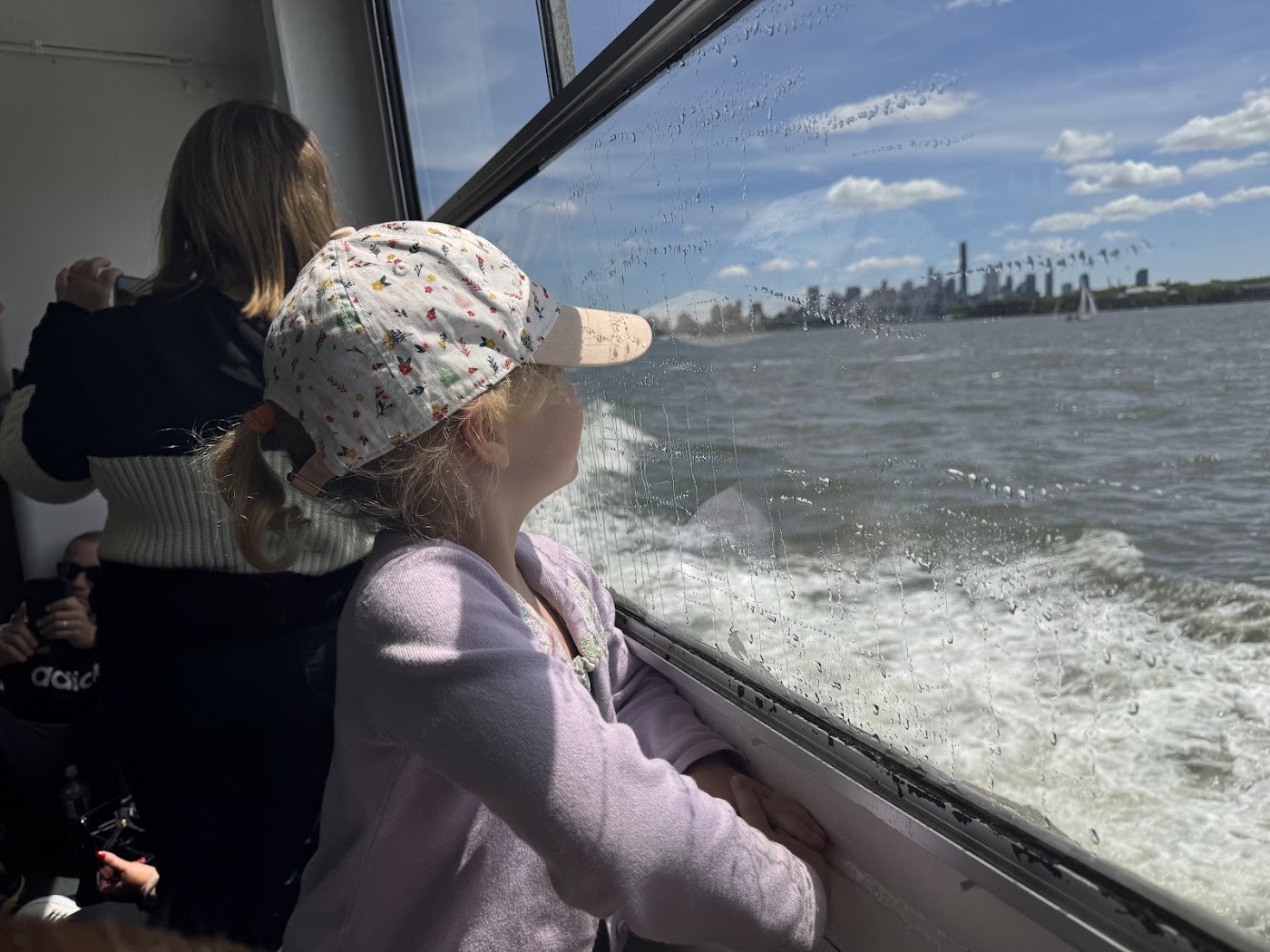 A girl in a sun hat looking back at the downtown skyline from a boat.