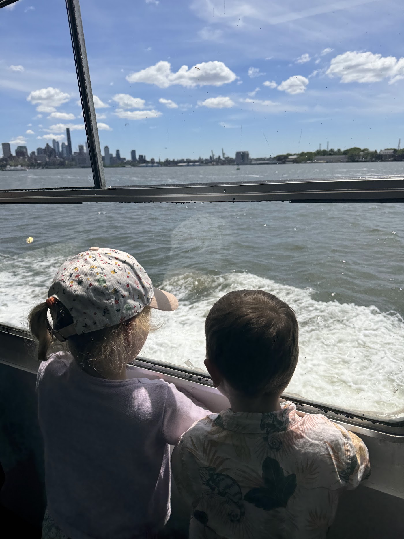 Two children at a ferry window looking at the churning white water behind the boat.