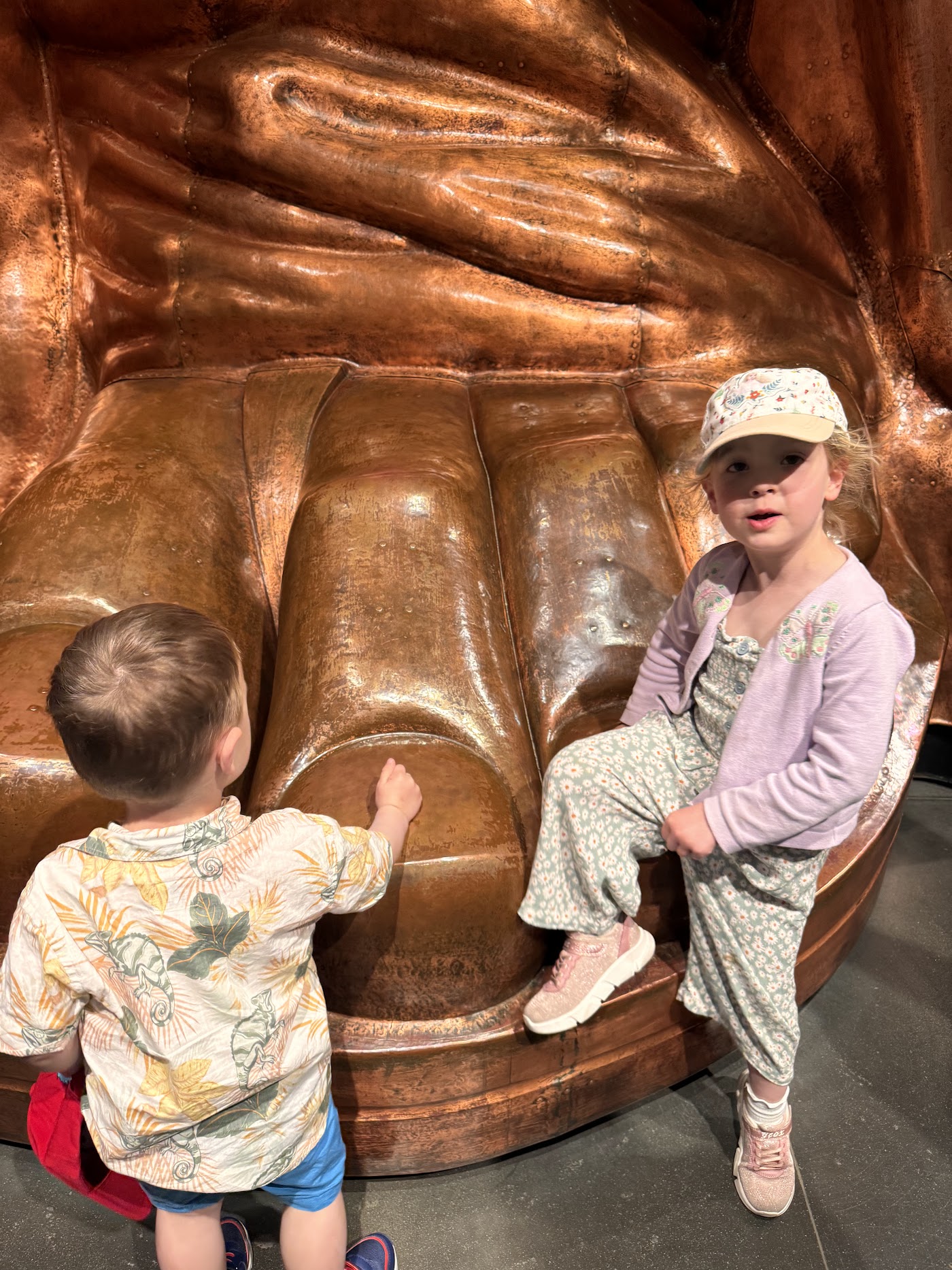 A child sitting beside a huge copper-colored face cast in a museum.