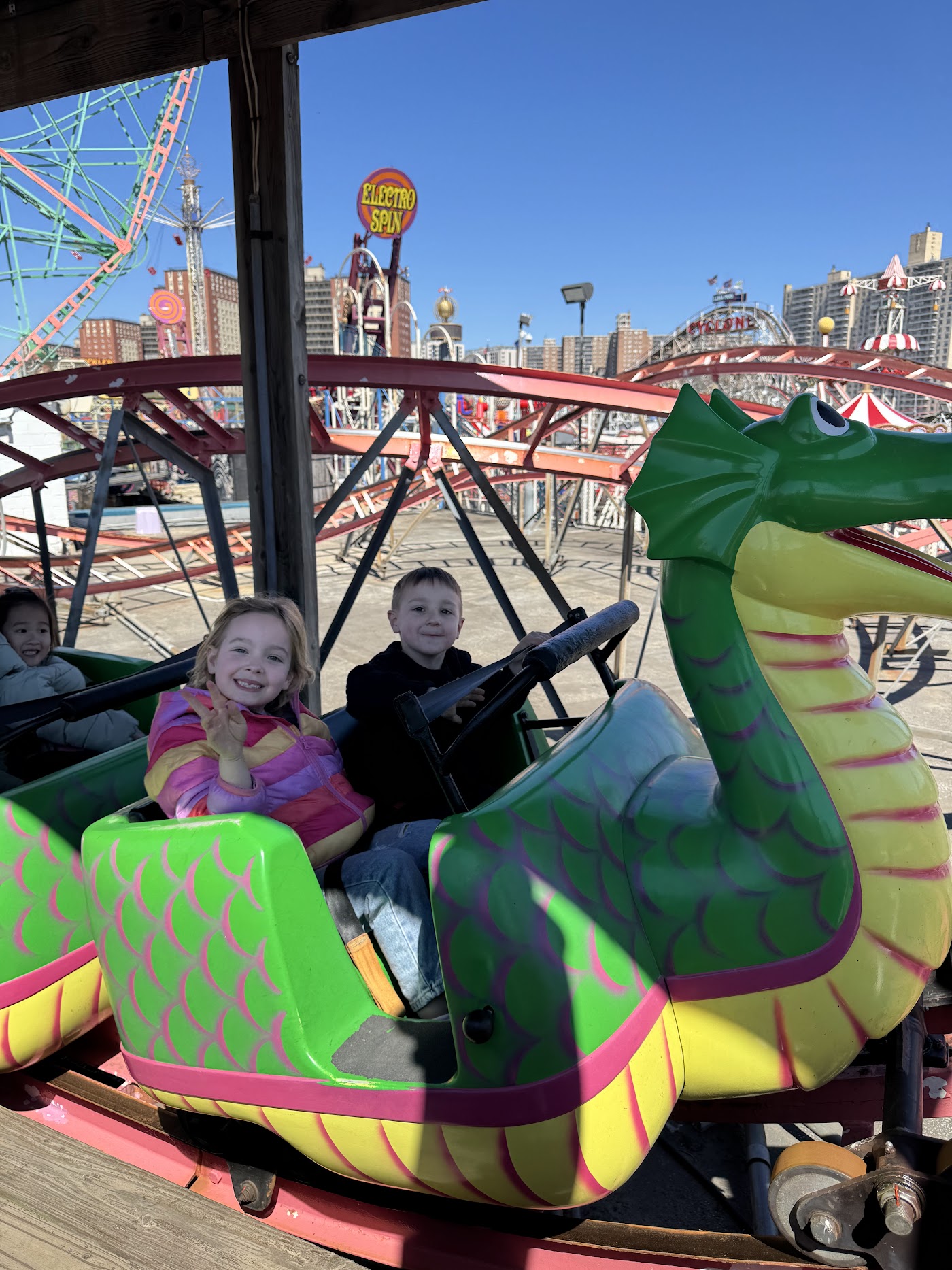A child on a green dragon ride car at an amusement park.