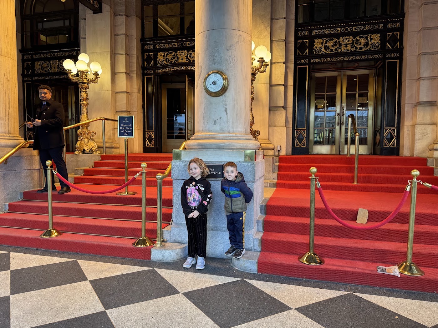 Two children at the foot of a wide red-carpeted staircase with brass rails.