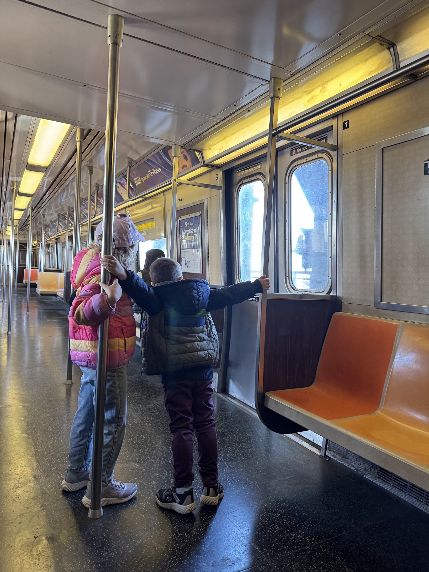 A child kneeling on an orange subway seat looking out of the window of an empty car.